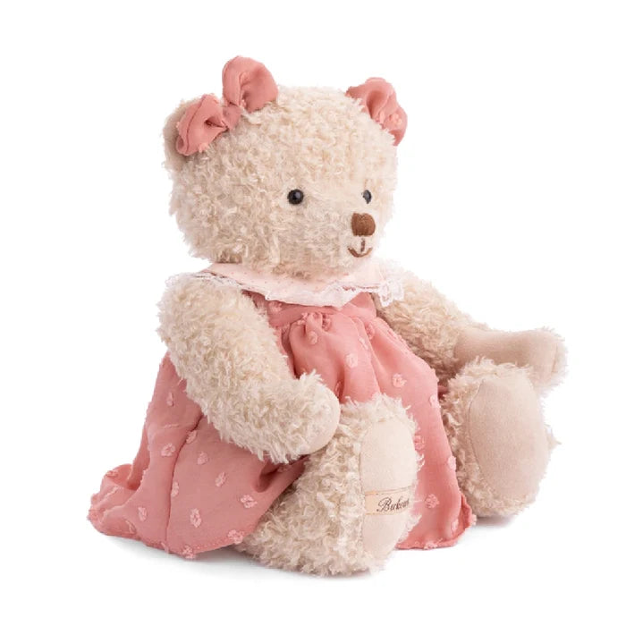 A teddy bear wearing a pink dress is positioned on a white background.