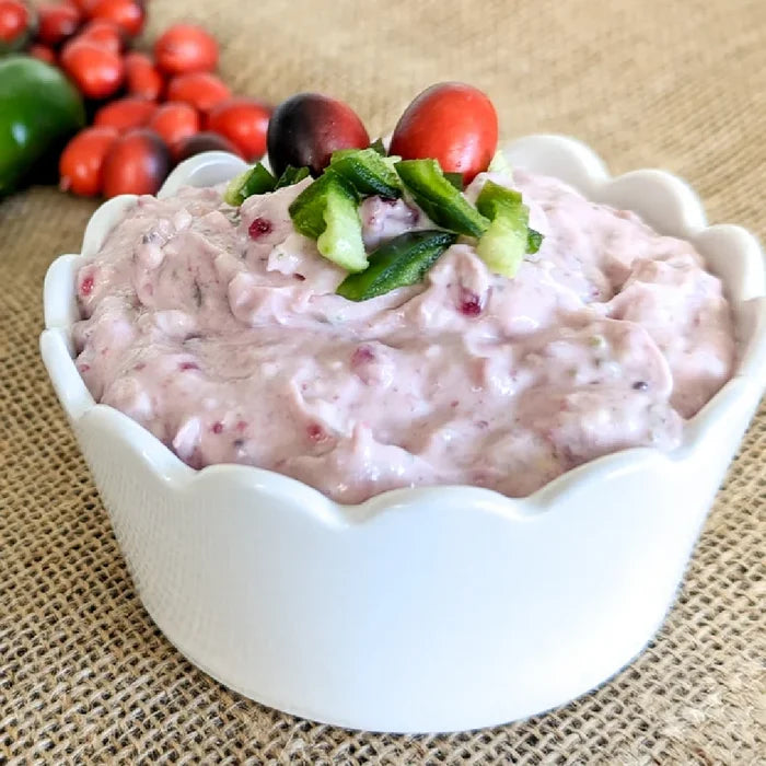 A vibrant cranberry jalapeño spread mix in a jar, featuring a rich red color and visible jalapeño pieces for flavor.
