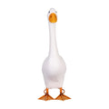 A white goose with an orange beak and orange legs standing on grass.