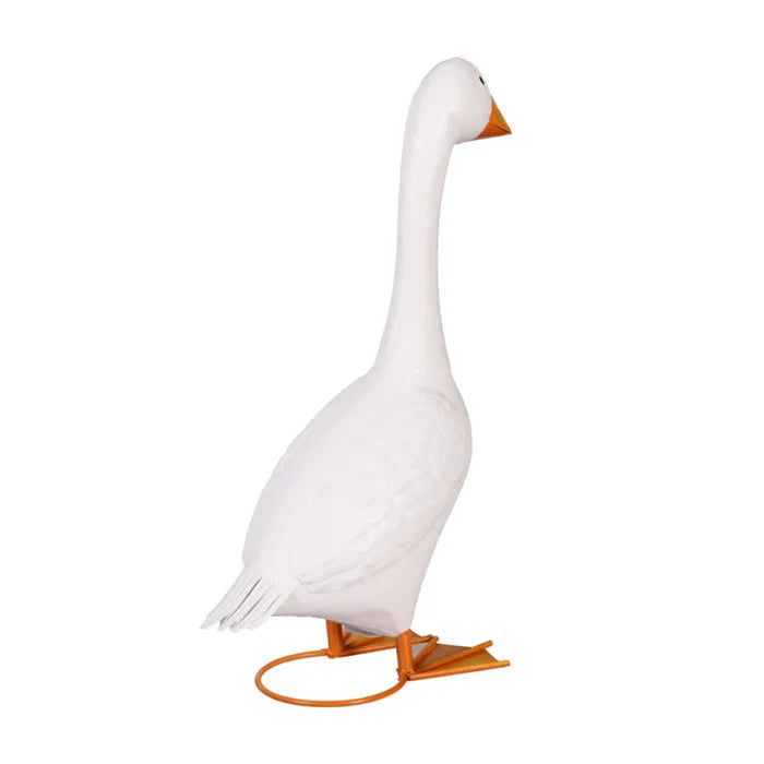 A white goose statue is featured on a porch, complemented by vibrant flowers nearby.