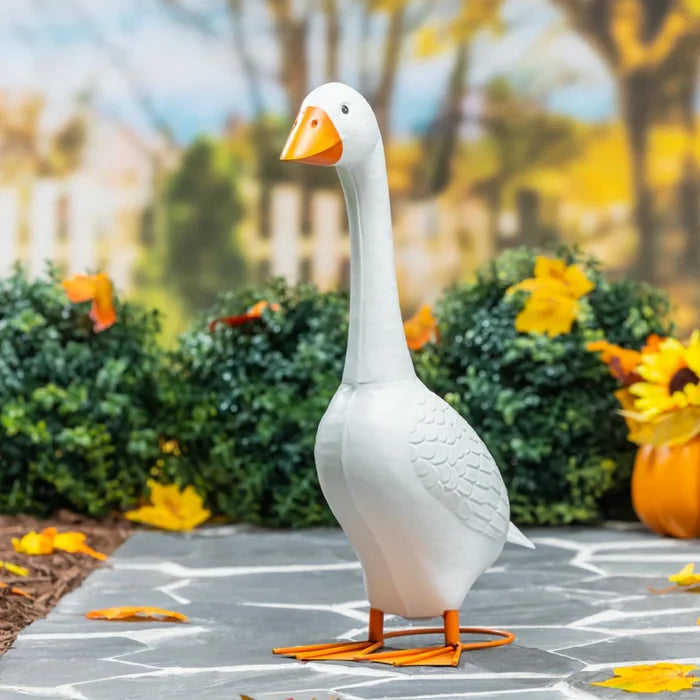 A white goose statue decorates a porch, with an array of flowers enhancing the scene.