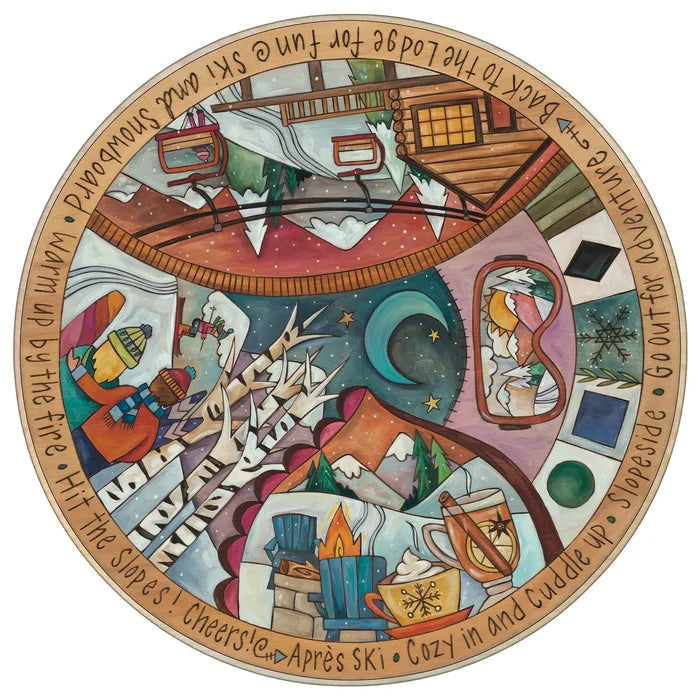 A circular illustrated lazy susan or featuring a whimsical winter mountain scene with cabins, snow, stars, a crescent moon, and handwritten-style text around the edge.