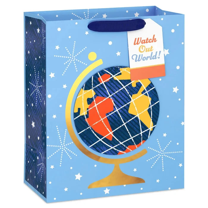 gift bag on a white background featuring a blue star-and-fireworks design with a colorful globe attachment on a gold stand and a “Watch Out World!” gift tag