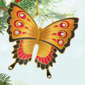 Butterfly-shaped ornament with gold, red, and black colors hanging on a Christmas tree.