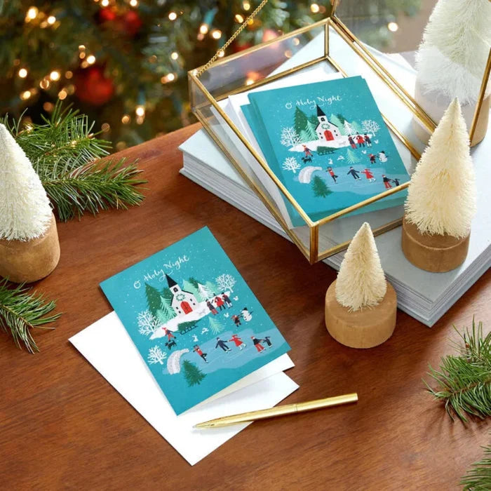 Christmas-themed greeting cards on a wooden table with decorative trees and lights.