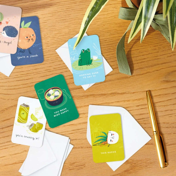 Colorful mini cards with illustrations on a wooden surface with a pen and plant.