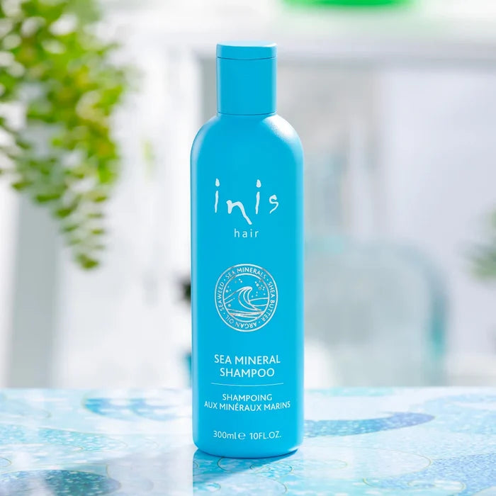 Blue shampoo bottle labeled 'inis hair' on a blue surface with a blurred natural background