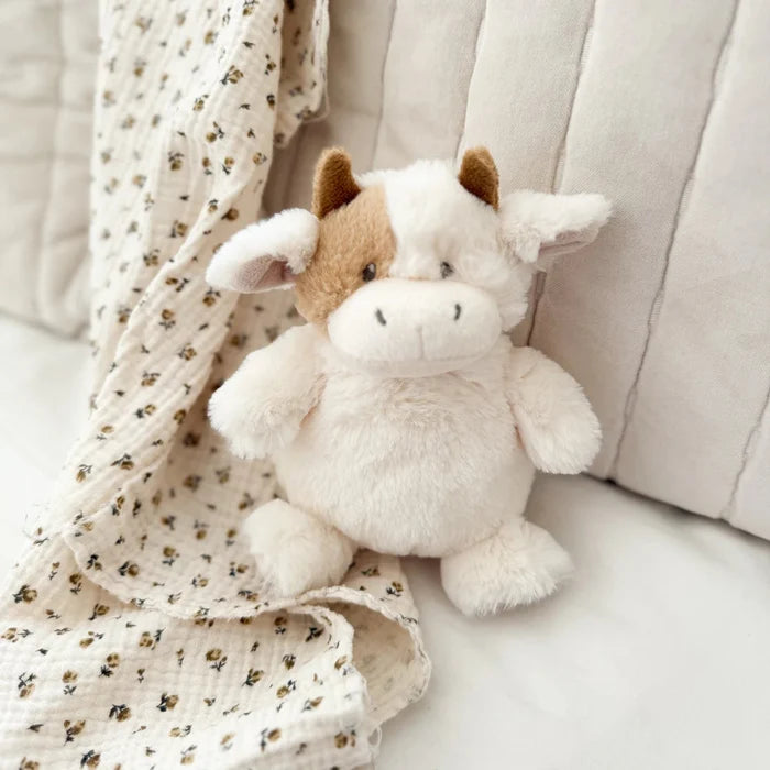 Plush cow sitting on a chair with a soft baby blanket draped behind it