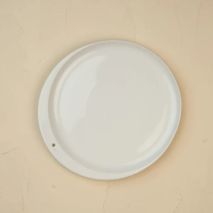 A white plate displayed against a beige wall, highlighting its simplicity and elegance.