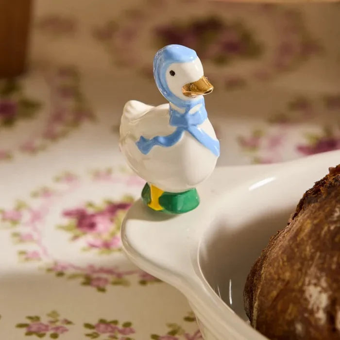 Mini Nora Fleming Mothe good Mini on a dish with bread in it, on a light floral background