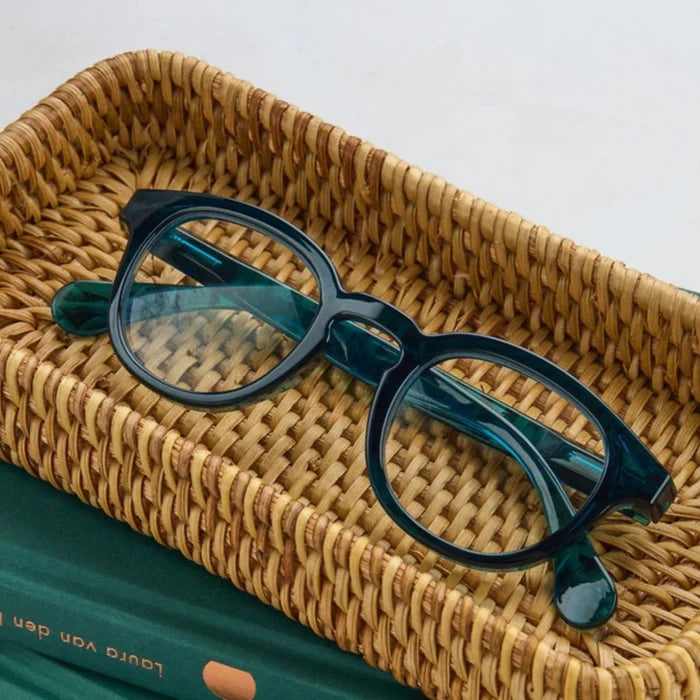 A pair of glasses rests in a basket atop a closed book, creating a cozy reading scene.