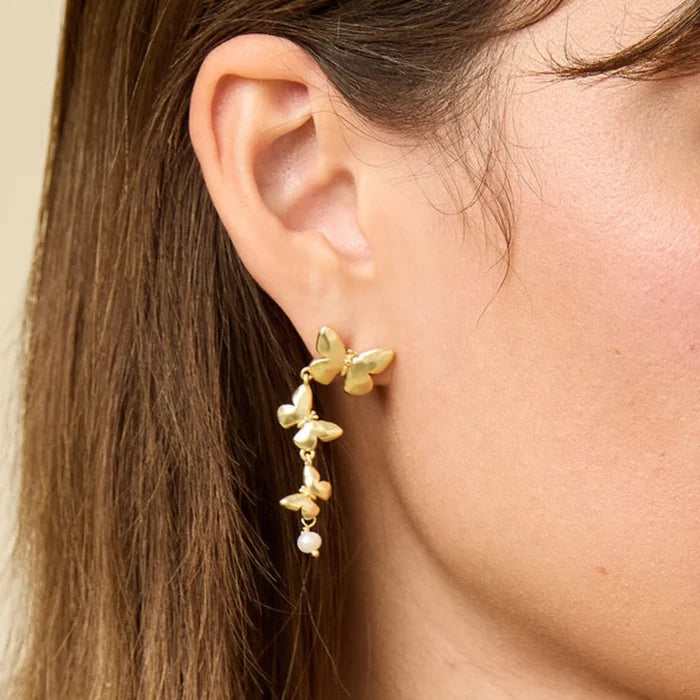 A close-up of a woman's ear wearing an elegant gold earring with floral designs and pearl accents.