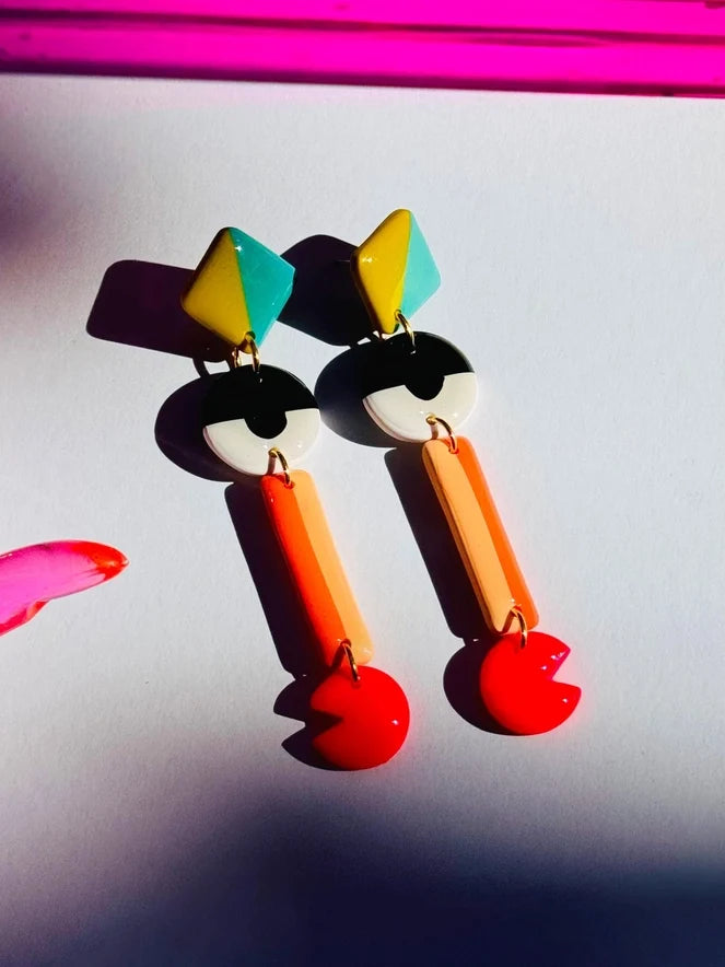 Colorful geometric earrings on a reflective surface with a pink border.