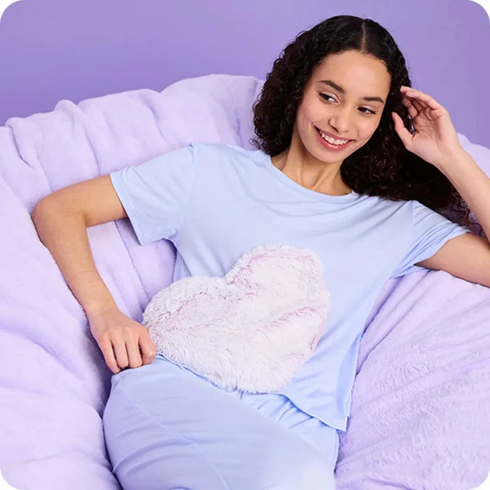 Woman sitting on a bean bag chair holding a heart-shaped pillow against a purple background