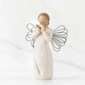 A willow tree angel holding a heart, symbolizing love and serenity in a peaceful outdoor setting.