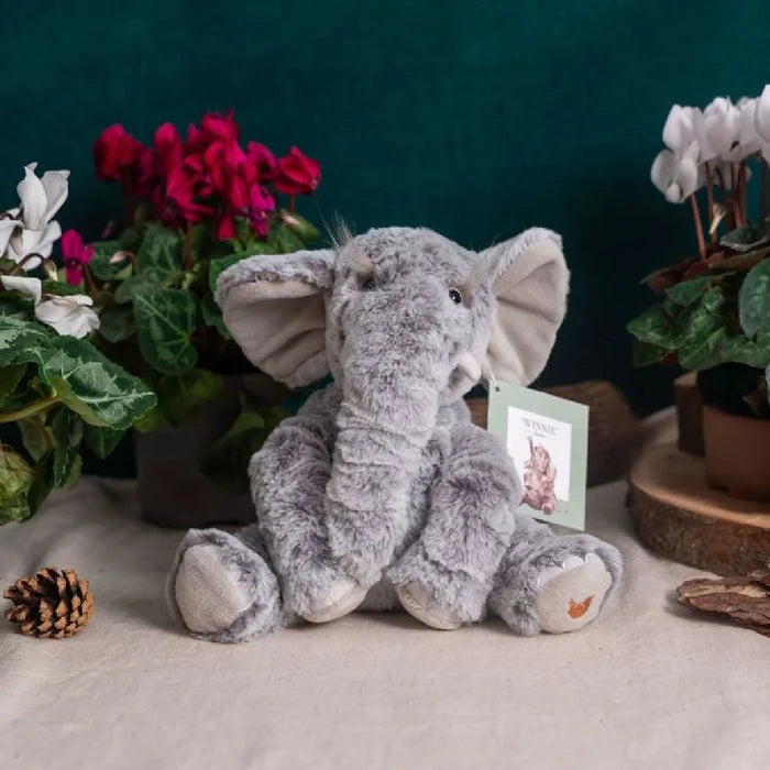 A stuffed elephant rests against a white backdrop, highlighting its cuddly appearance and friendly expression.