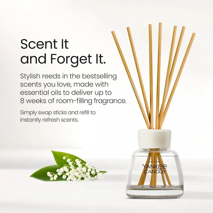 Yankee Candle reed diffuser bottle with wooden reeds, shown on a clean white background with promotional text and a small lily of the valley sprig.